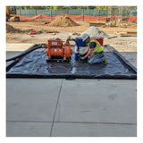 A construction worker in safety gear kneels on an UltraTech Foam Wall Model Containment Berm – Light-Duty, using equipment with an orange pump at a construction site with dirt piles and fencing in the background.