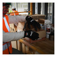 A person wearing MCR Safety Ninja Ice Insulated Work Gloves N9690Q (12 pairs), an orange vest, and a face covering is handling a cardboard box on a busy worktable in a warehouse or construction setting.