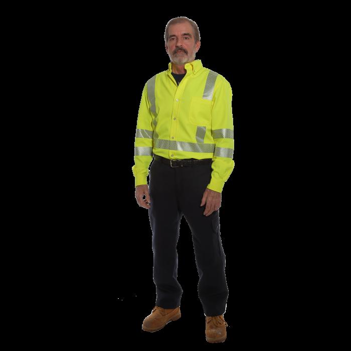 A man wearing an NSA DRIFIRE FR Hi-Vis Work Shirt in a vibrant yellow with reflective stripes, paired with black pants and brown boots, stands facing forward. The plain black background highlights the distinctiveness of his attire.