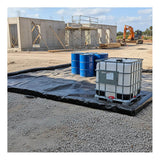 An UltraTech Foam Wall Model Containment Berm - Light-Duty by UltraTech holds blue barrels and a white IBC tank on a gravel construction site, with an unfinished building and excavator in the background.
