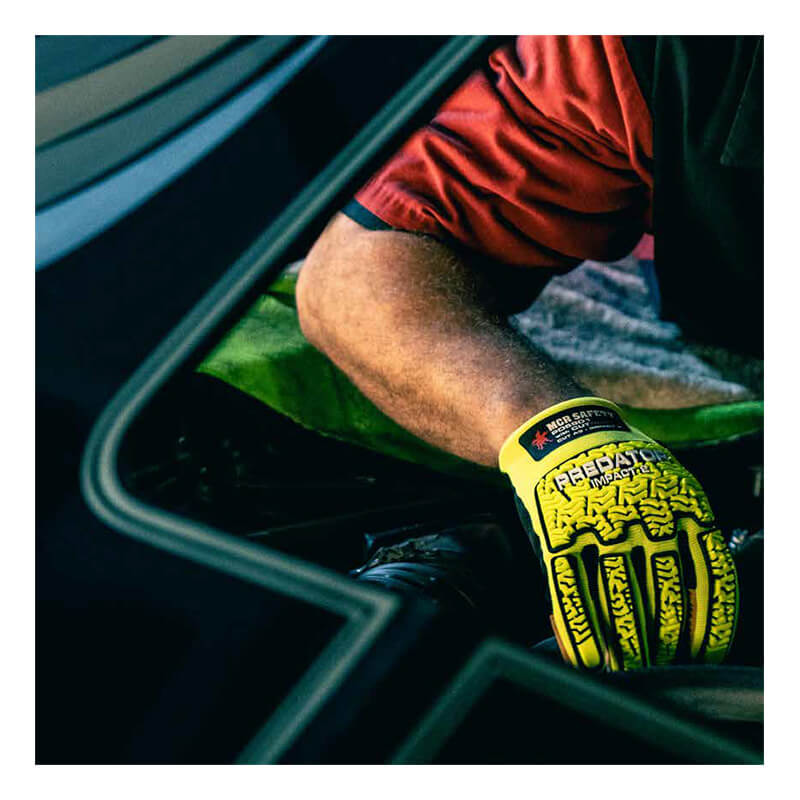 A person wearing a red shirt and MCR Safety Predator Hi-Vis Mechanics Gloves w/360 HyperMax PD6901 works on a car, seen through the open door.