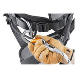 A person wearing tan gloves is connecting a locking carabiner to a Petzl ASTRO BOD FAST International Harness C083BA0_. The grey harness, featuring black and grey straps, is designed for climbing or safety purposes.