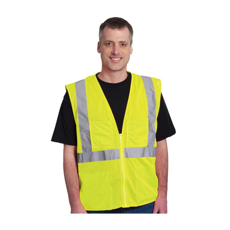 A person wearing the PIP ANSI Type R Class 2 Four Pocket Mesh Vest 302-MVGZ4P, a bright yellow hi-vis vest from PIP - Protective Industrial Products, smiles at the camera. The vest's breathable mesh design and reflective silver tape create a striking contrast against the plain white background.