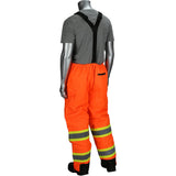 A mannequin displays the PIP Ripstop Insulated Two Tone Bib Overalls 318-1780 by Protective Industrial Products, featuring high-visibility orange work pants with reflective stripes and black suspenders over a gray T-shirt. This Class 3 apparel includes ripstop insulated material, two horizontal reflective bands near the cuffs, and a black pocket on the back.