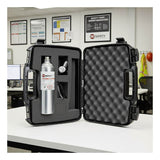 A black hard-shell case with foam padding is open on a desk, displaying the PK Safety RKI Equivalent Calibration Kit PKCalKit-RKI and accessories inside. In the background are safety posters and a high-visibility vest. Brand: PK Safety.