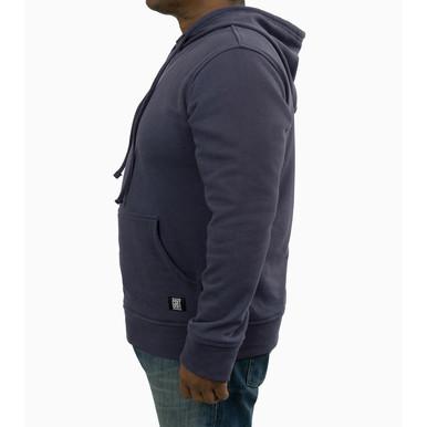 A person wearing a dark blue GRIT FR Pullover Hoodie by GRIT FR Workwear and jeans is standing sideways against a plain white background. The hoodie, perfect for electrical work apparel, includes a front pocket and drawstrings.