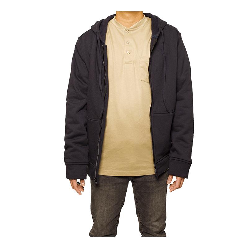 A person is wearing a black GRIT FR Zip-Up Hoodie over a beige henley shirt and brown pants. Their hands are relaxed at their sides, embodying the flame-resistant ethos of GRIT FR Workwear's commitment to worker safety. The image is taken against a plain white background.