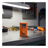 An AimSafety CO Single Gas Monitor PM100-CO rests on a metal workbench in a workshop, surrounded by tools and wires under the glow of an overhead lamp.