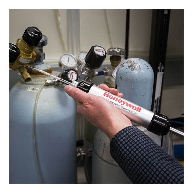 A person uses a BW Technologies by Honeywell Piston Hand Pump and colorimetric gas detection tubes to sample gas from a cylinder with gauges and valves in a laboratory.