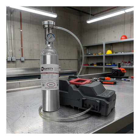 An RKI Instruments SDM-3R Calibration Station Bundle is connected via tubing to a metal gas cylinder with a pressure gauge, all set up on a stainless steel workbench in an industrial lab. The area is equipped with calibration tools and surrounded by shelves, various equipment, and safety helmets in the background.