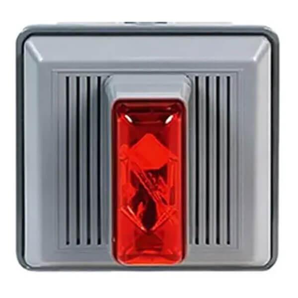 A square grey switch from RKI Instruments' Fixed Systems, known as the RKI 4 Wire Strobe/Horn for outdoor panel mounting at 120 VAC, features a textured surface with a prominent red rectangular button in its center. Distinctive ridged vertical lines flank the button, enhancing its robust design.