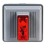 A square grey switch from RKI Instruments' Fixed Systems, known as the RKI 4 Wire Strobe/Horn for outdoor panel mounting at 120 VAC, features a textured surface with a prominent red rectangular button in its center. Distinctive ridged vertical lines flank the button, enhancing its robust design.