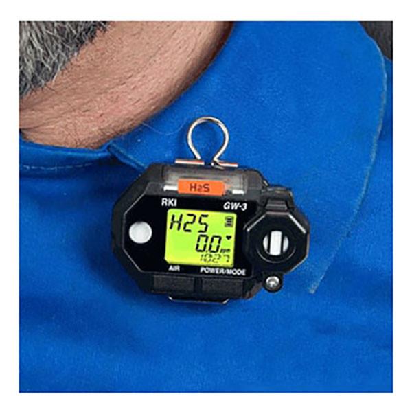 An RKI Instruments GasWatch 3 H2S Single Gas Monitor 73-0022 is clipped onto a blue shirt, displaying hydrogen sulfide (H2S) concentration at 25 ppm. This device features a digital screen for precise environmental monitoring, making it ideal for use in refineries.