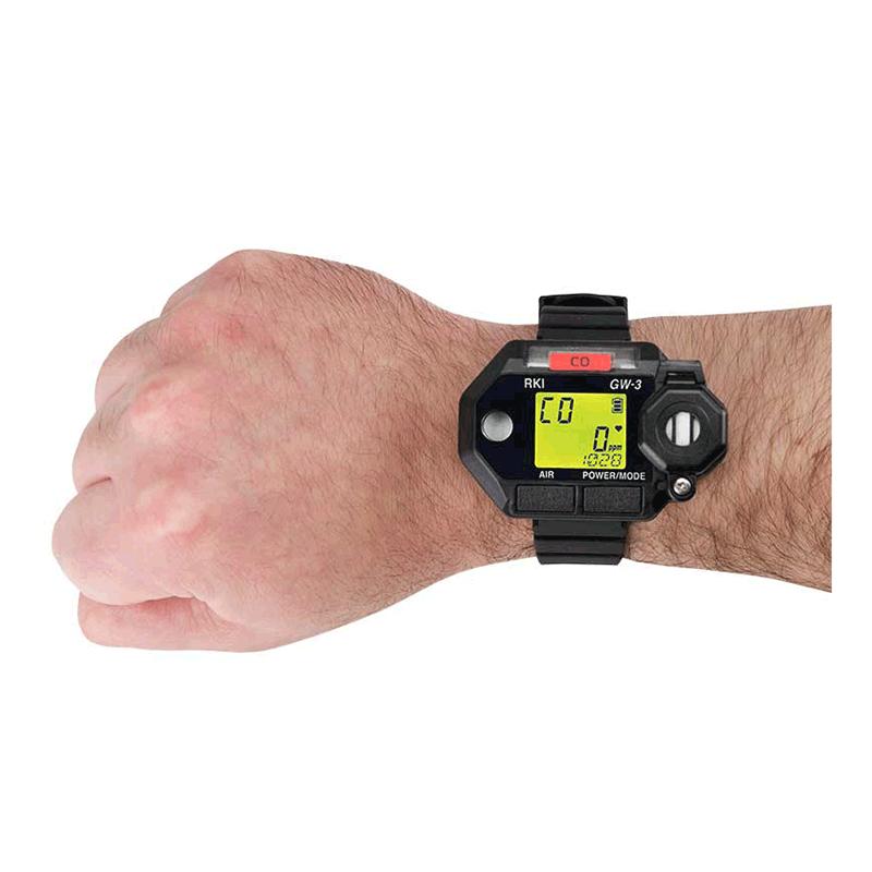 A person's hand wearing the RKI Instruments GasWatch 3 CO Gas Personal Monitor 73-0023 is shown. This black digital watch features a large rectangular display that provides various numerical readings, serving as an integrated gas monitor. The adjustable band is securely fastened around the wrist, and the device has an impressive IP-66/68 rating for durability.