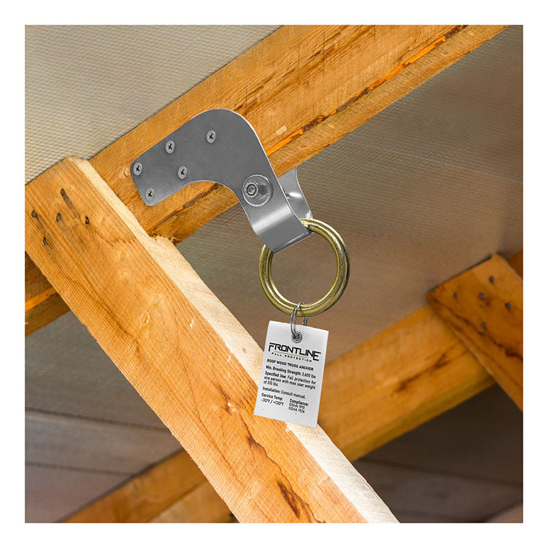The Frontline Roof Wood Truss Anchor ROWT18 by Frontline Fall Protection features a large circular ring and attaches securely to wooden rafters for reliable fall protection. A white information tag is attached to the ring.