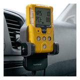 The WatchGas SST Range Wireless Car Charger SST-CAR-CHG, a yellow gas detector with digital display, is mounted on a car dashboard holder labeled "FastCharge" and doubles as a wireless charger. The screen shows numbers and text inside the vehicle.