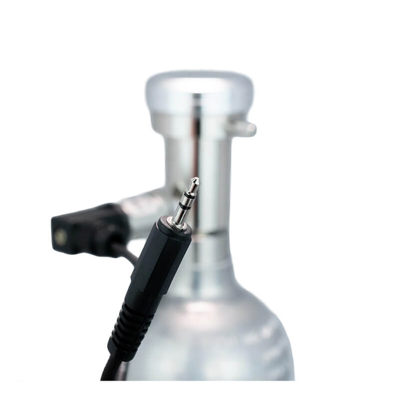 A close-up of a 3.5mm audio jack held in front of a metallic component, likely part of the WatchGas Demand Flow Regulator with Pressure Sensor Valve by WatchGas, with a blurred background.