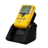 A yellow WatchGas detector with a digital display rests on the WatchGas Induction Cradle Charger - Single Desktop w/Adapter, designed for charging SST4 and SST5 industrial gas detectors.