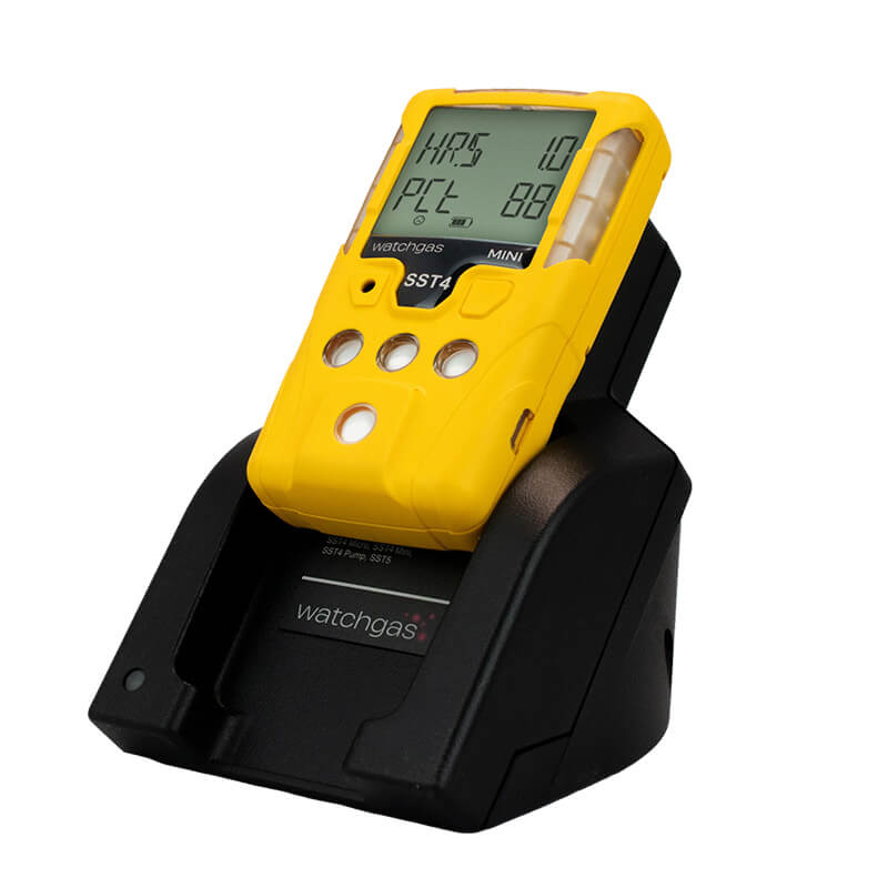 A yellow handheld gas detector with a digital display rests on the WatchGas Induction Cradle Charger - Single Desktop w/Adapter, designed for industrial use and compatible with SST4 and SST5 detectors. The charger features the WatchGas brand logo.