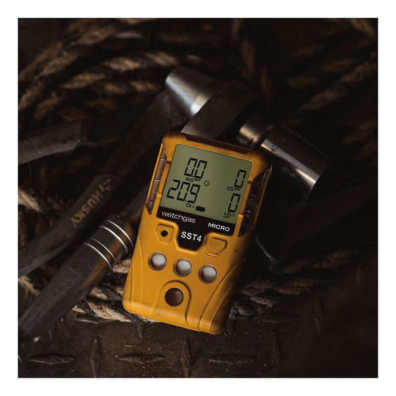 A WatchGas SST4-MICRO Diffusion 4-Gas Detector by WatchGas, featuring a digital display reading "209" and “0” for different gases, sits on a dark surface next to two hammers and a coiled rope, highlighting industrial safety.