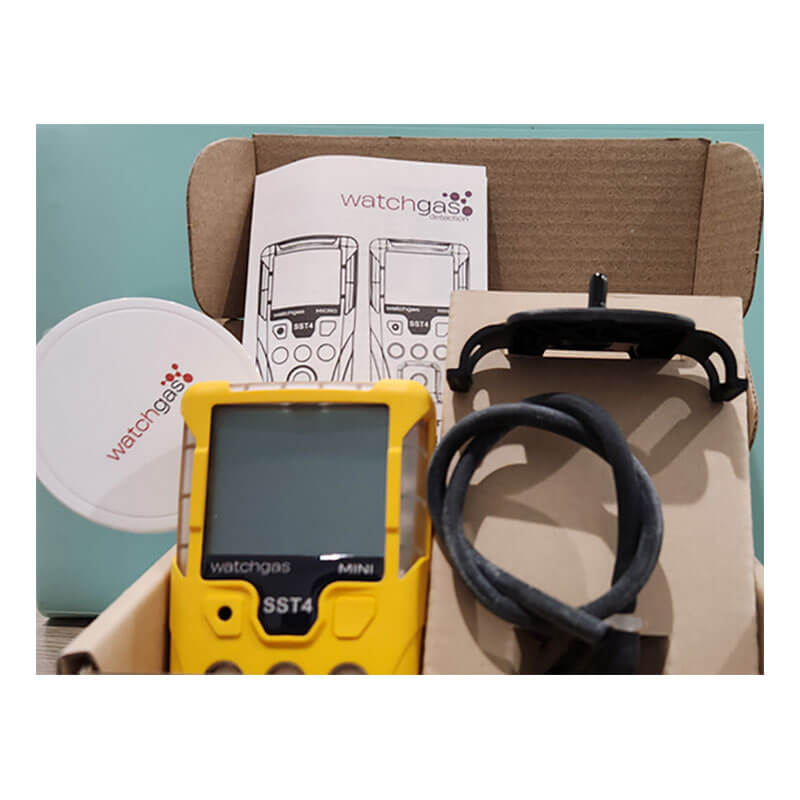 The WatchGas SST4-MINI Diffusion 4-Gas Detector, with a black cable, mounting clip, manuals, and a round white lid featuring the WatchGas logo, is neatly arranged in an open box for efficient gas monitoring.