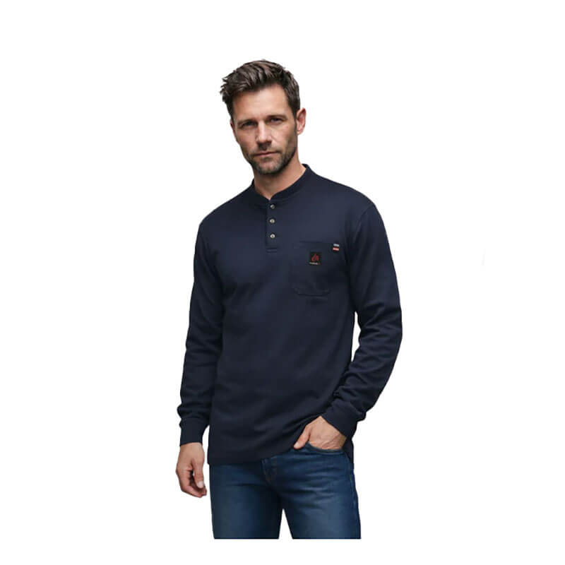 A man wears a dark blue ForgeFR Forge FR Henley MFRHNLY-004 with a small chest pocket and blue jeans, standing against a plain white background.