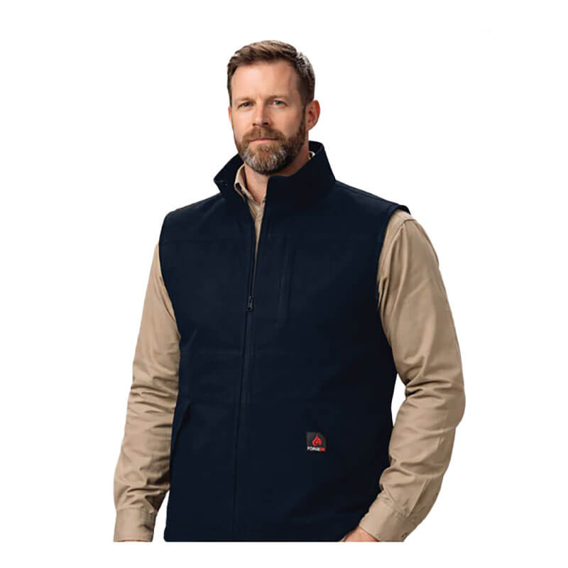A bearded man wears the ForgeFR Forge FR Canvas Duck Vest MFRVST-001, a black flame-resistant vest, over a beige long-sleeve shirt while standing against a plain white background.