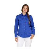 A woman with a single braid wears the ForgeFR Forge FR Ladies Solid Snap Shirt LFRSLD, a bright blue flame resistant workwear shirt with chest pockets, paired with white pants against a plain white background.