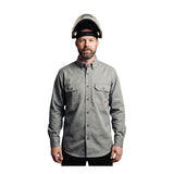 A bearded man wearing the ForgeFR Forge FR Solid Button Shirt MFRLB2PS024 in light gray with chest pockets faces forward. He has a clear safety helmet with a black band, and the background is plain white.