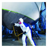 Wearing a Dupont Tyvek 400 D TY127S WB Coverall Suit, a person equipped with a pink respirator uses a tool to sand or clean the underside of a large boat inside an industrial facility.