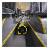 A Euramco RamFan UB20 18VDC blower, colored yellow, sits on the floor between rows of empty patterned seats inside a bus, facing toward the front.