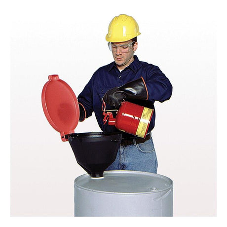 A person equipped with safety gear, such as a yellow hard hat, goggles, and gloves, is meticulously pouring liquid from a red safety can into an UltraTech Burp-Free Model Drum Funnel 065_ by UltraTech International atop a large drum. They maintain focus on the task, ensuring attention to detail and chemical resistance.