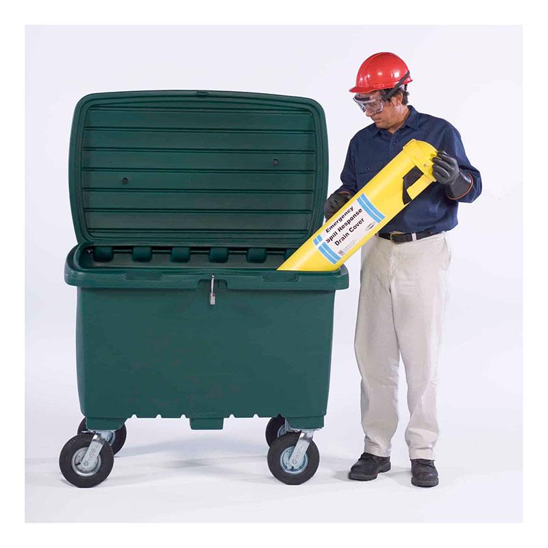 A person wearing a red hard hat and safety goggles is placing a long, yellow object labeled "For Disposal Spill Containment" into an UltraTech International UltraTech Utility Box 086_, which is large, green, equipped with wheels, and has an open lid. The background is plain white.