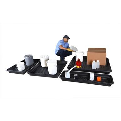 A person wearing a blue uniform is managing a container on an UltraTech Utility Tray 103_ by UltraTech International, crafted from heavy-duty polyethylene. Several black trays designed for spill containment are holding various containers, such as buckets and bottles, against a white background.