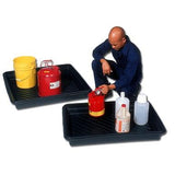 A person in blue overalls sits next to two UltraTech International Utility Tray 103_ units on the floor. One tray, crafted for spill containment with heavy-duty polyethylene, holds a red container and a yellow bucket, while the other contains several bottles. The individual is handling the red container.