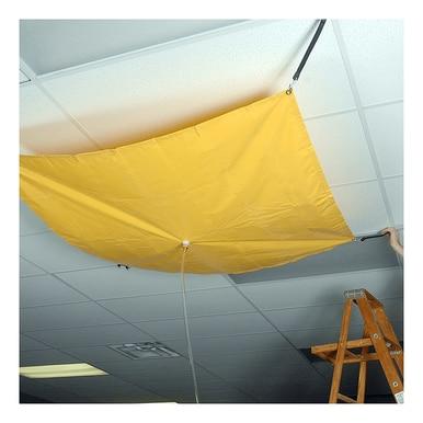 An UltraTech Roof Drip Diverter 178, made of yellow vinyl-coated fabric by UltraTech International, is suspended from the ceiling to efficiently manage water from a leak. A hose extends from its center for drainage. A person on a wooden ladder adjusts the setup among ceiling tiles and fluorescent lights to ensure no leak emergency escalates.