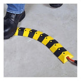 A person's boot steps over the UltraTech Sidewinder System with Endcaps 18_0, manufactured by UltraTech International, showcasing its modular design on the concrete floor. This system has a curved structure that neatly covers an orange cable and features a black and yellow color scheme.