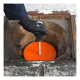 A person wearing a black glove is carefully handling the UltraTech Drain Plug 211_ from UltraTech International, which is attached to an orange disc, lowering it into a rusted, circular opening. The gray and weathered surface around the entrance ensures an efficient spill response solution.