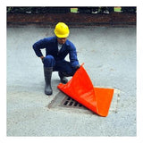 A worker in a yellow hard hat, blue coveralls, and rubber boots kneels on the ground, positioning an UltraTech Drain Seal 213_ from UltraTech International over a storm drain on a paved surface, demonstrating an essential part of the stormwater management program.