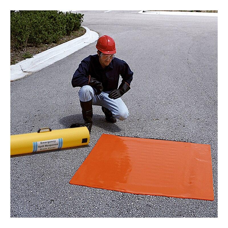 A person wearing a red hard hat and protective gear kneels on asphalt next to an unfolded orange UltraTech Drain Seal 213_, integral to the emergency response plan. A yellow tube labeled "Emergency Spill Response" lies nearby, with shrubbery visible in the background, ensuring effective stormwater management.