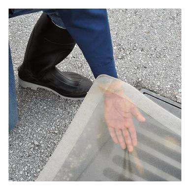 A person wearing black boots and blue clothing inspects a storm drain on pavement. Their hand hovers near the UltraTech Clear Model Drain Seal 220_, a component of the spill response drain cover system from UltraTech International.