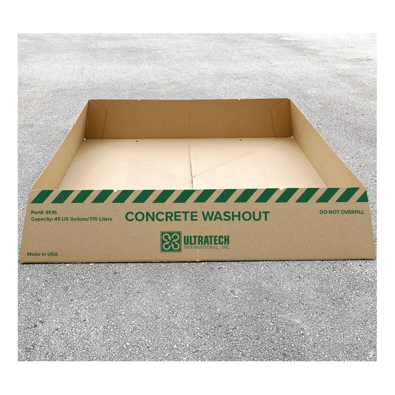 An UltraTech International "UltraTech Concrete Washout Berms - Economy Model 351_" cardboard box with a capacity of 45 US gallons/170 liters rests on the gray pavement. It is adorned with green diagonal stripes and features clear instructions not to overfill, ensuring EPA compliance for efficient concrete waste disposal.