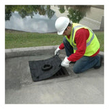 A worker wearing a red shirt, yellow safety vest, white gloves, and a hard hat kneels on the sidewalk to lift a black cover from a storm drain. Utilizing the UltraTech Inlet Guard Plus 916_ for drain protection from UltraTech International, the scene features reflective water surfaces and grassy surroundings in the background.