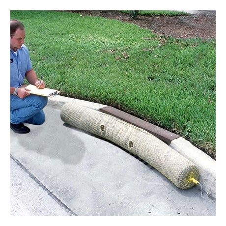 A man kneels on a sidewalk, writing on a clipboard. In front of him, an UltraTech Gutter Guard from UltraTech International is placed at the curb's edge for stormwater protection. Made from recycled synthetic fibers, it effectively shields the storm drain. The area is bordered by grass.