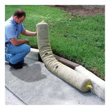 A person wearing a blue shirt kneels on a concrete path next to a green grassy area, adjusting the UltraTech International's UltraTech Gutter Guard, crafted from recycled synthetic fibers, at the curb's edge. This ensures stormwater protection by preventing debris from entering the storm drain.