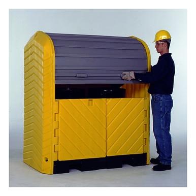 Wearing a yellow hard hat and gloves, an individual stands beside the UltraTech International UltraTech Hard Top P2 Plus Spill Pallet 961_, lifting its lid. This large spill containment unit features vertical grooves and dual front doors, set against a simple indoor backdrop.