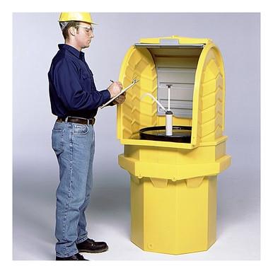 A worker wearing a blue shirt, jeans, and safety gear is writing on a clipboard next to an UltraTech Hard Top P1 Plus Spill Pallet 964, an outdoor containment unit shaped like a yellow barrel with an open top and pump handle.