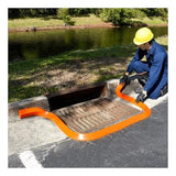 A person wearing a yellow hard hat and blue overalls is kneeling beside a storm drain, carefully placing an UltraTech Spill Berm from UltraTech International as a spill barrier. The scene takes place outdoors near a grassy area with a body of water in the background, emphasizing the importance of spill response.