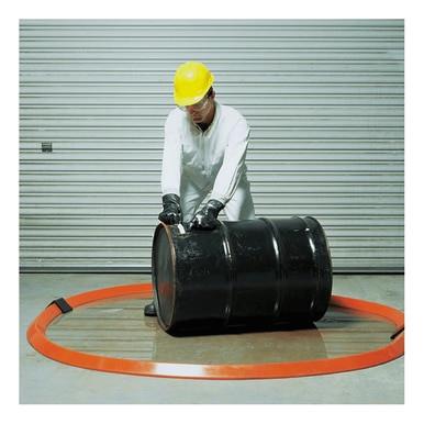 Clad in protective gear and a yellow helmet, a worker expertly navigates a large black barrel within the UltraTech Spill Berm, 10 Foot Length, from UltraTech International. This takes place inside an orange containment barrier on the slippery surface, with the scene framed by a closed metal garage door in the background.