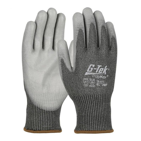 A pair of PIP G-Tek PolyKor gloves features a gray design with black textured palms and fingers that provide cut resistance for enhanced protection. The back is adorned with the "G-Tek PolyKor" logo and product details. These gloves have dark gray cuffs with brown edging, and they are also touchscreen compatible.